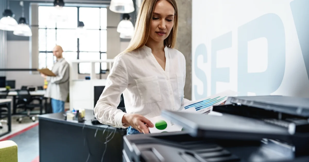 Young professional woman scanning colourful charts at a modern office printer.